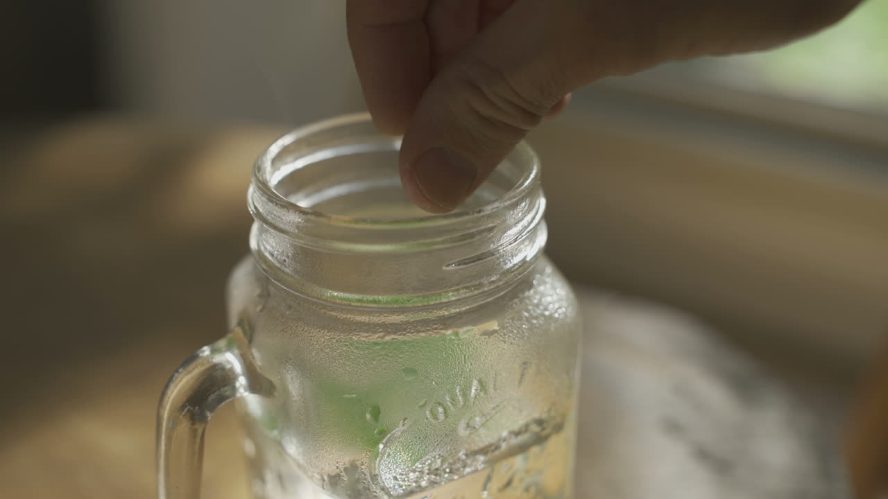 Adding mint and tea leaves into glass mug with boiling water