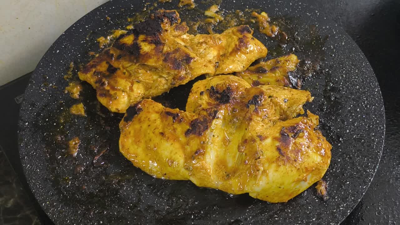 Chicken meat, marinated with spices, is grilled on a flat, non-stick pan. The spices sizzle, releasing a delicious aroma. Close-up shot shows the chicken browning perfectly on the grill