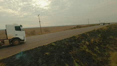 Feuer-Neben-Der-Straße,-LKW-Fahrt-Neben-Rauchwolken,-Ackerlandanbau,-Brandrodungsplantage,-Drohnen-Übersichtsaufnahme,-Straßenbrand,-4K-Aufnahme