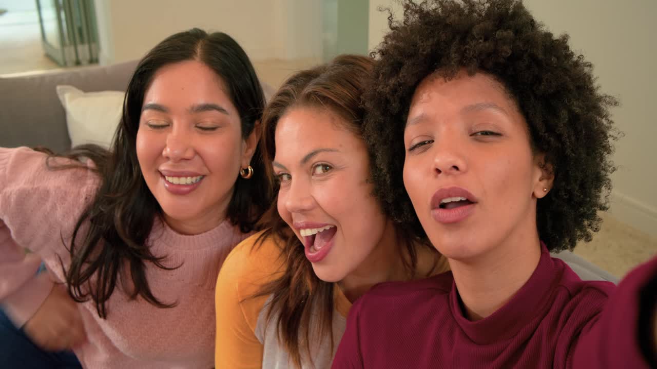 Diverse amiche sul divano che guardano lo smartphone, imbronciate, che ridono, che posano, che fanno il segno della pace e che arricciano le labbra