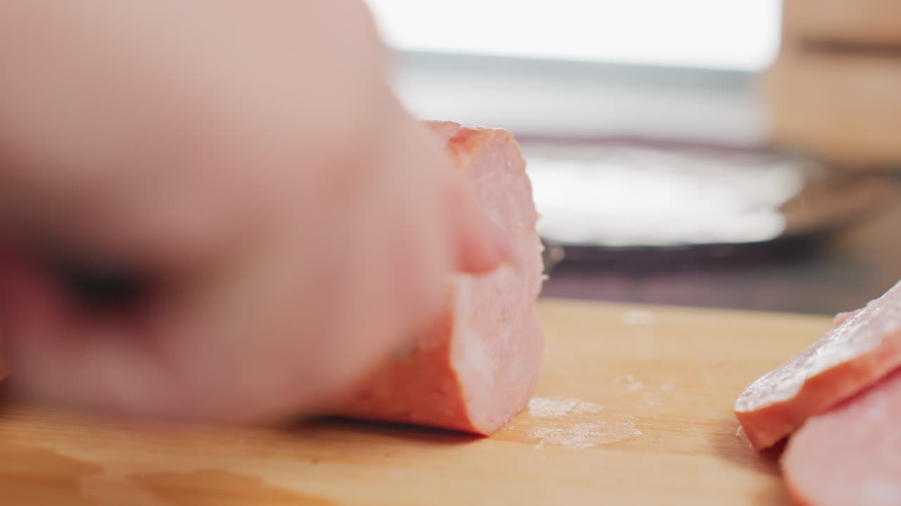 close up rear view person slicing round pink meat on wooden cutting board using sharp kitchen knife, soft blur background, showing delicate food preparation and natural indoor kitchen environment