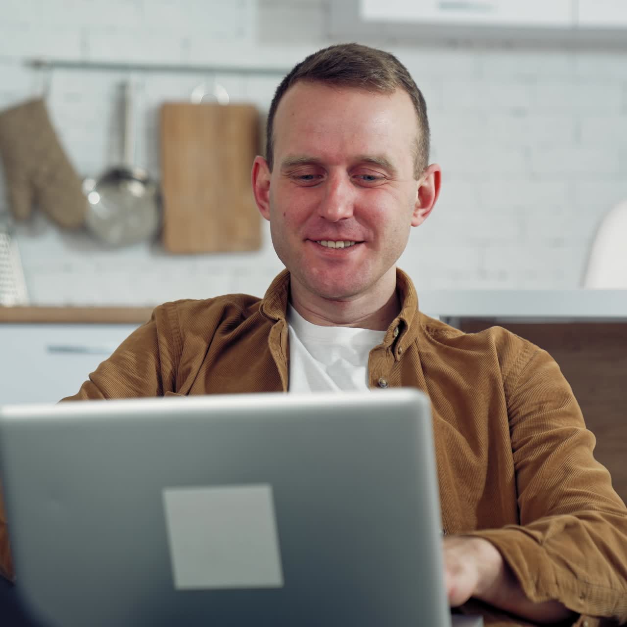 Young man freelancer using laptop in the kitchen. Happy man having a conversation through the laptop. Online working from home. Remote work from home during coronavirus quarantine