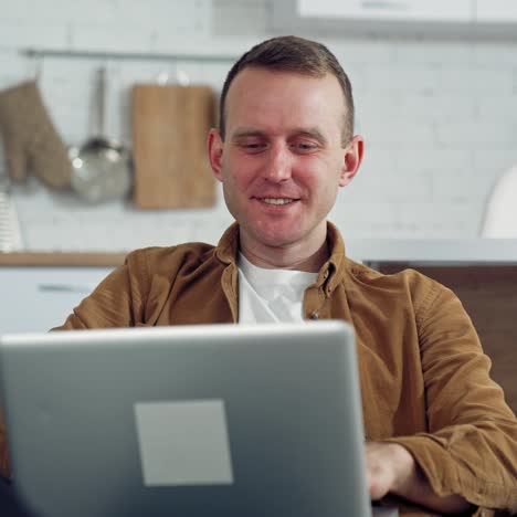 young man freelancer using laptop in the kitchen. happy man having a conversation through the laptop. online working from home. remote work from home during coronavirus quarantine