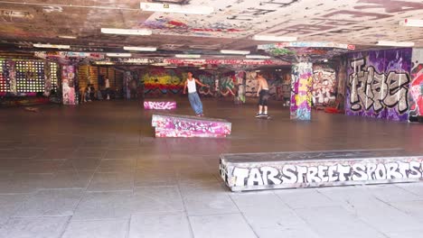 skateboarders performing tricks in graffiti-covered park