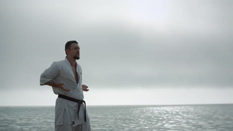 taekwondo man training strength near calm sea. sportsman practicing martial arts