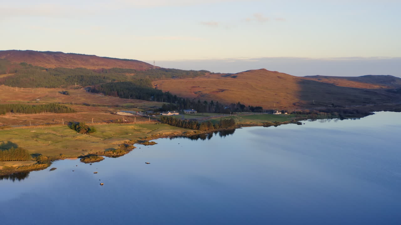 Aerial high orbit across lakeshore edge of Lough Bofin and surrounding hills, the lake’s natural beauty under a clear sky, Connemara, Galway, Ireland