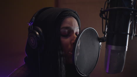 a mixed race female recording artist sings into the microphone while recording her bands song in a professional recording studio