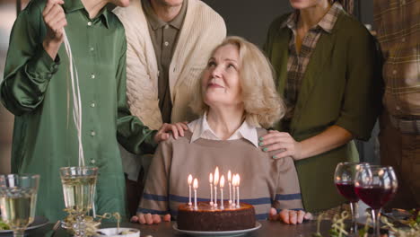 retrato de una anciana soplando velas en un pastel de cumpleaños durante una celebración con su familia en casa
