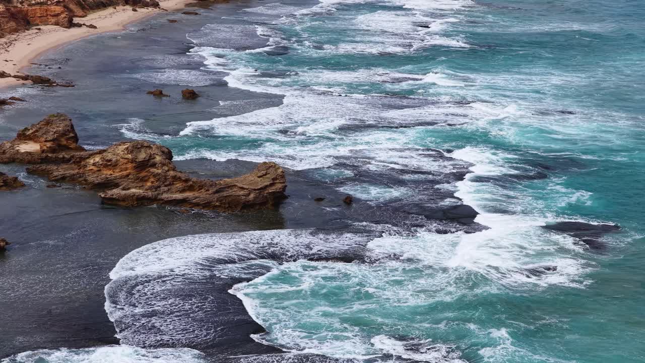 Aerial view of turquoise waves breaking over coastal rock formations, natural daylight, smooth camera movement