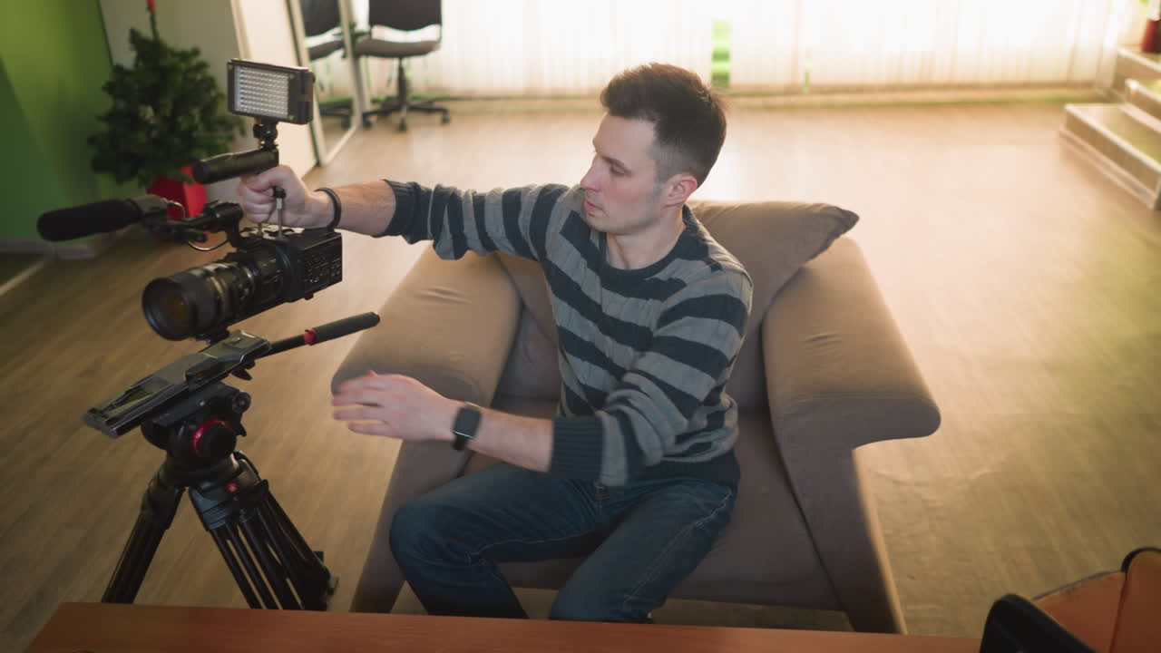 Studio guy adjusting camera lens, focused on preparing gear for video shoot in home studio. Lighting, microphone, and camera equipment on table for upcoming production