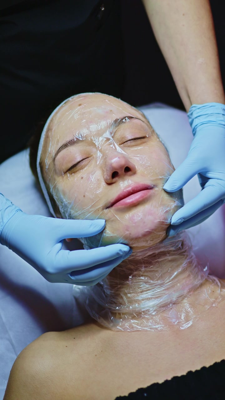 Donna che riceve un trattamento viso in una spa durante una sessione di cura della pelle nelle ore serali con un'estetista che applica una maschera