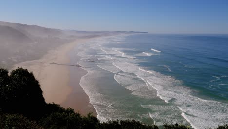 view from mountain over wide stretch of gorgeous beach with waves rolling on to it