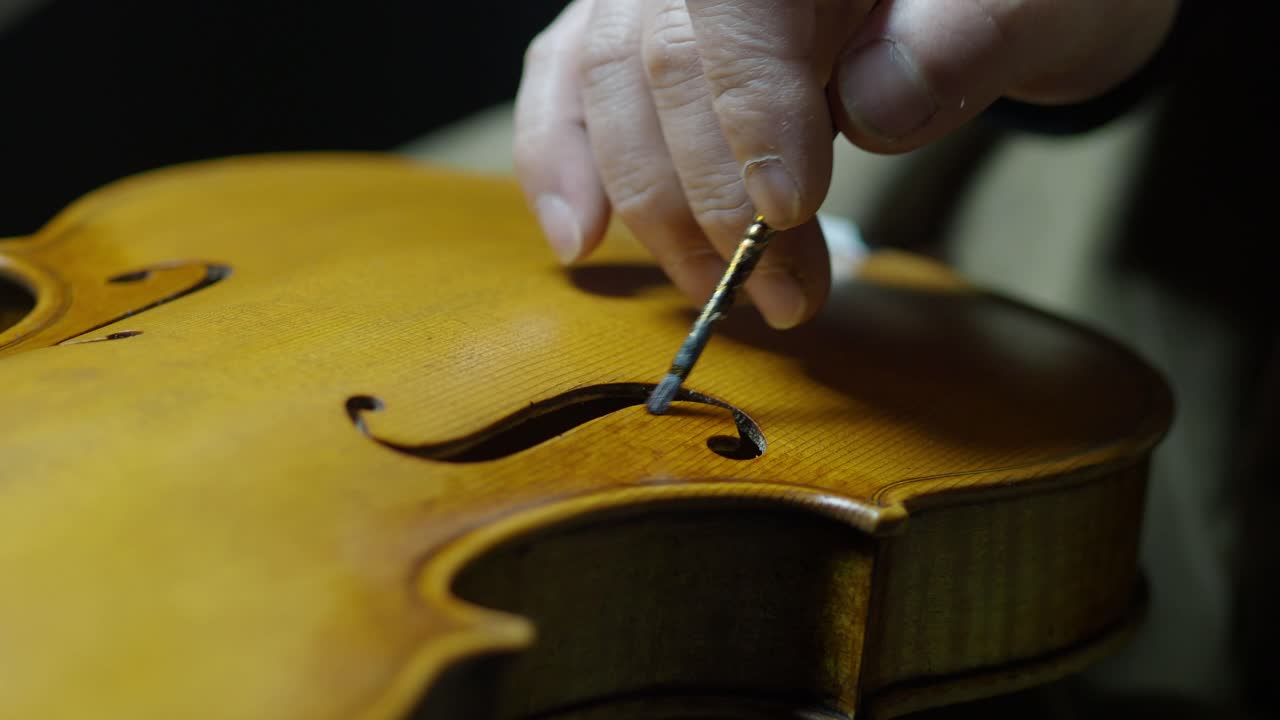 Skilled Craftsman Carefully varnishig top plante near F-Hole of a Vintage Violin with paintbursh and finger tamponing