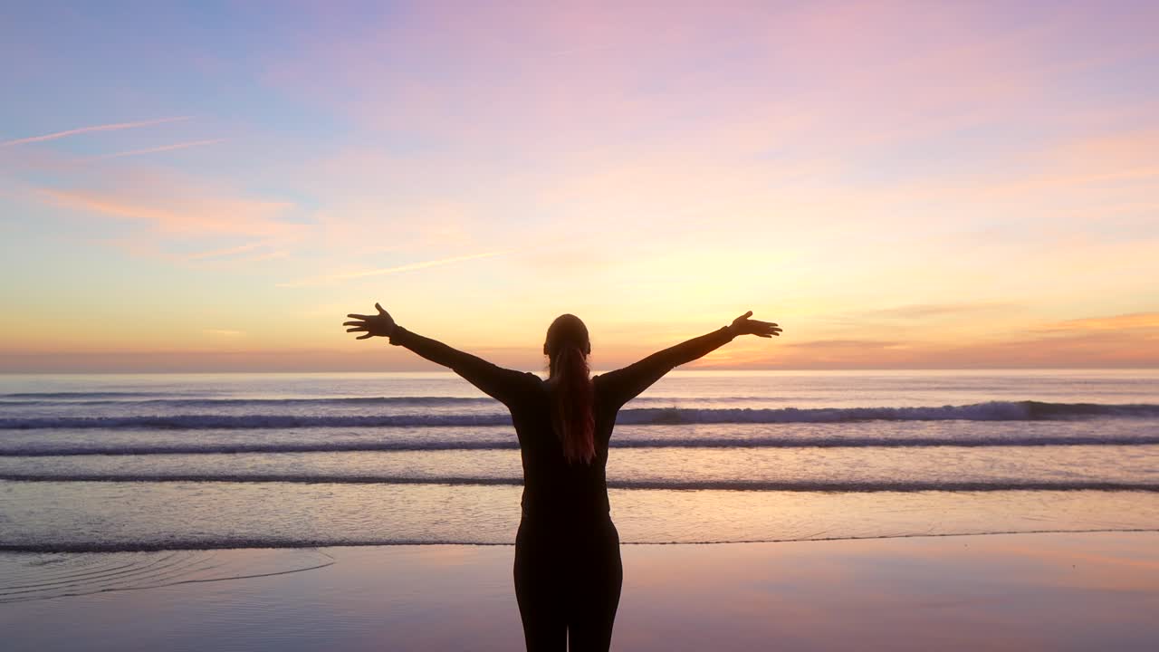 mujer extendiendo los brazos y viendo el mar al amanecer con zoom out