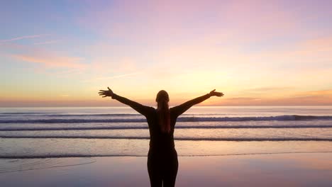 Mujer-Extendiendo-Los-Brazos-Y-Mirando-El-Mar-Al-Amanecer-Con-Zoom-Out.