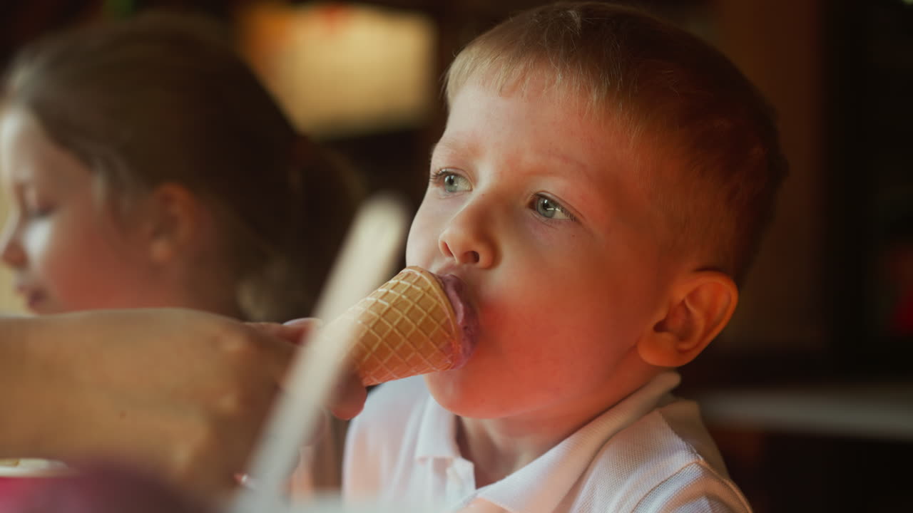 madre alimenta al niño pequeño con helado de chocolate descansando en la cafetería en cámara lenta. lindo hijo pequeño muerde helado en la mano de los padres en el restaurante de primer plano
