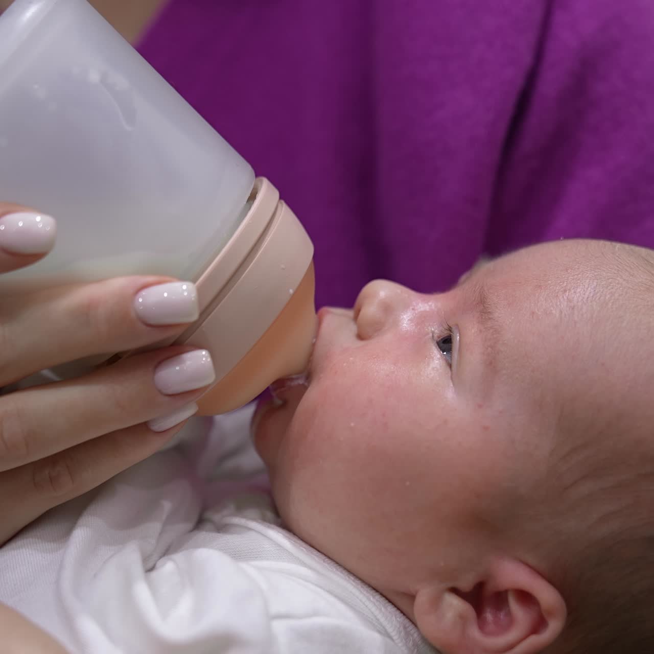 Little infant baby lying on mother's hands. Tiny baby suckling milk from the plastic bottle. Close up shot