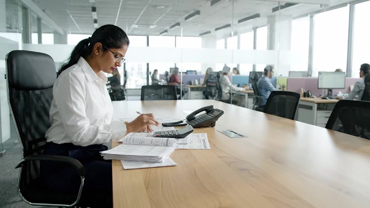 Mulher profissional focada analisando dados financeiros com calculadora em um ambiente de escritório moderno, demonstrando produtividade e concentração durante o horário de trabalho.