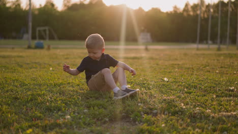 little boy kicks legs sitting on lush grass on playground