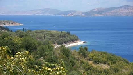 view of forested rocky cliffs on corfu island, with the blue sea and tall mountains in the background