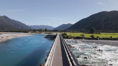 one lane bridge crossing blue fresh water stream in mountainous landscape of new zealand