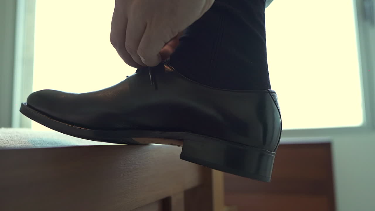 Close-up of man tying formal black leather shoes, style, elegance, and personal grooming