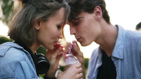 closeup view of attractive young couple in the park standing and and sharing milkshake drinking it together using two straws