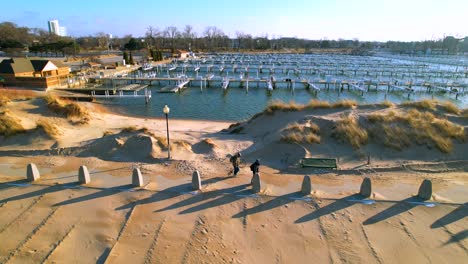 Two-fishermen-walk-along-pier-with-boats-moored-on-sunny-winter-day