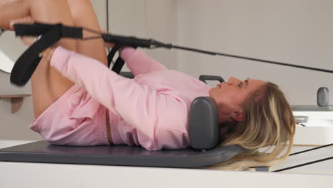 sporty blonde strong adult woman doing reformer pilates. slow motion