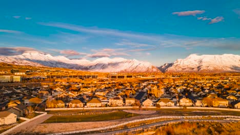 Schneebedeckte-Berge-über-Einer-Stadt-Im-Tal-Bei-Sonnenuntergang---Hyperzeitraffer-Aus-Der-Luft