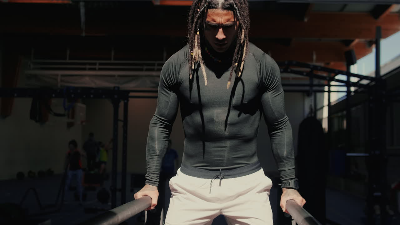 Målbevidst mand med dreadlocks udfører dips i et fitnesscenter