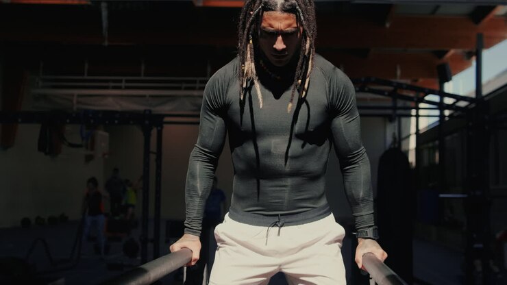 Målbevidst mand med dreadlocks udfører dips i et fitnesscenter