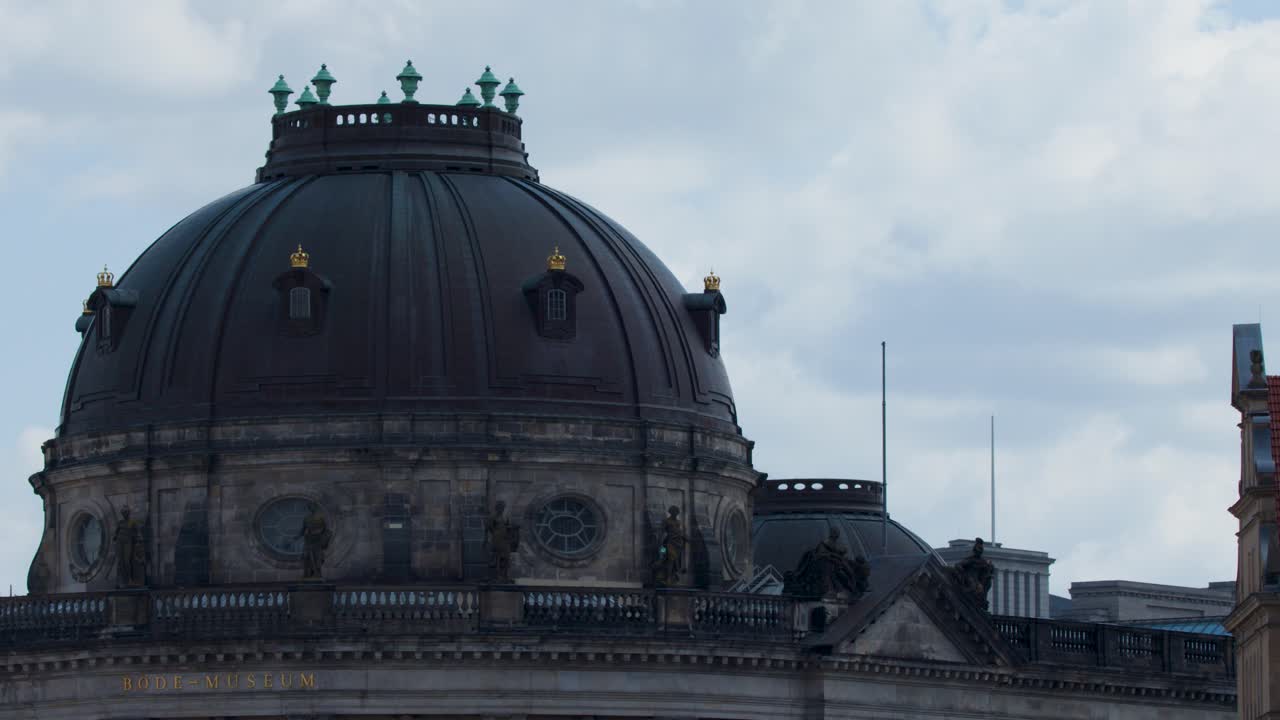Camera slowly pans across Bode Museum dome under daylight, highlighting historic architecture and cloudy sky