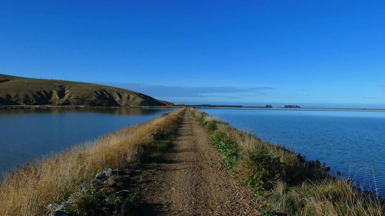 pov caminando sobre una vía férrea en desuso entre una laguna y un lago en un hermoso y tranquilo día de mediados de invierno - pequeño sendero ferroviario fluvial