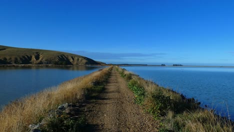 POV-Spaziergang-Auf-Einer-Stillgelegten-Eisenbahnstrecke-Zwischen-Lagune-Und-See-An-Einem-Schönen,-Ruhigen-Tag-Mitten-Im-Winter-–-Kleiner-Flussbahnweg