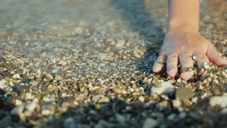 a woman's hand is looking for something in shallow pebbles on the edge of the sea 4k video