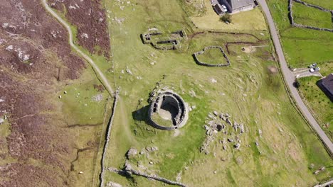 Drone-shot-from-a-birds-eye-view-perspective-of-the-Carloway-Broch-with-surrounding-stone-black-houses