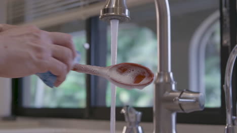 un hombre caucásico está limpiando una cuchara roja en la cocina de una casa