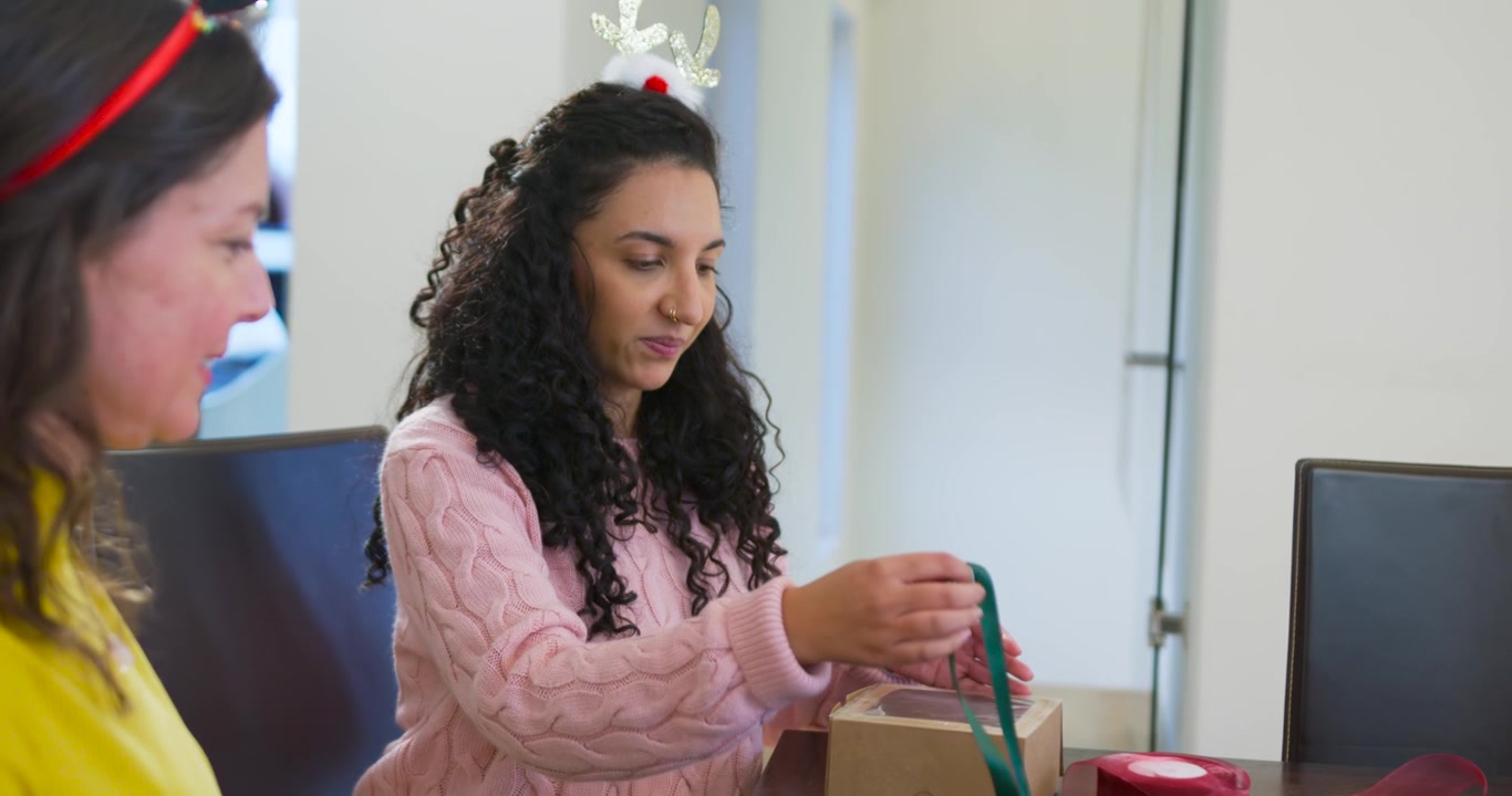 Mulheres afro-americanas dobrando caixas, amarrando fita verde à mesa enquanto preparam presentes de Natal.