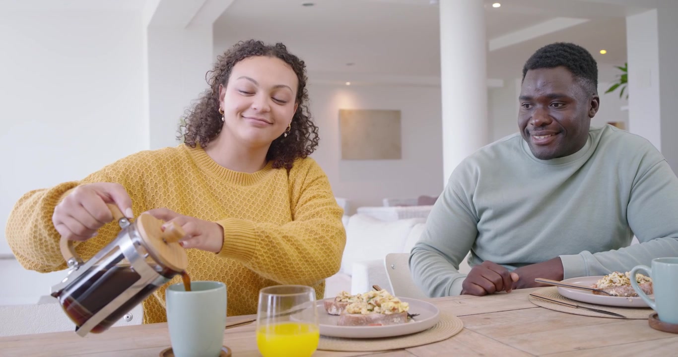 Pareja diversa compartiendo el desayuno en la mesa, mujer alcanzando la prensa, sirviendo café y abrazándose