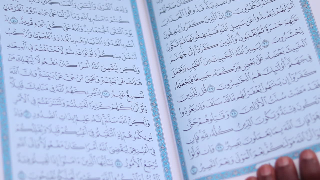 Close up of Quran being held open by a man, decorated pages filled with sacred texts are visible