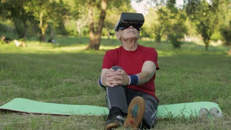 hombre anciano con casco de auricular vr sentado en una estera deportiva. entrenamiento deportivo en línea para personas mayores