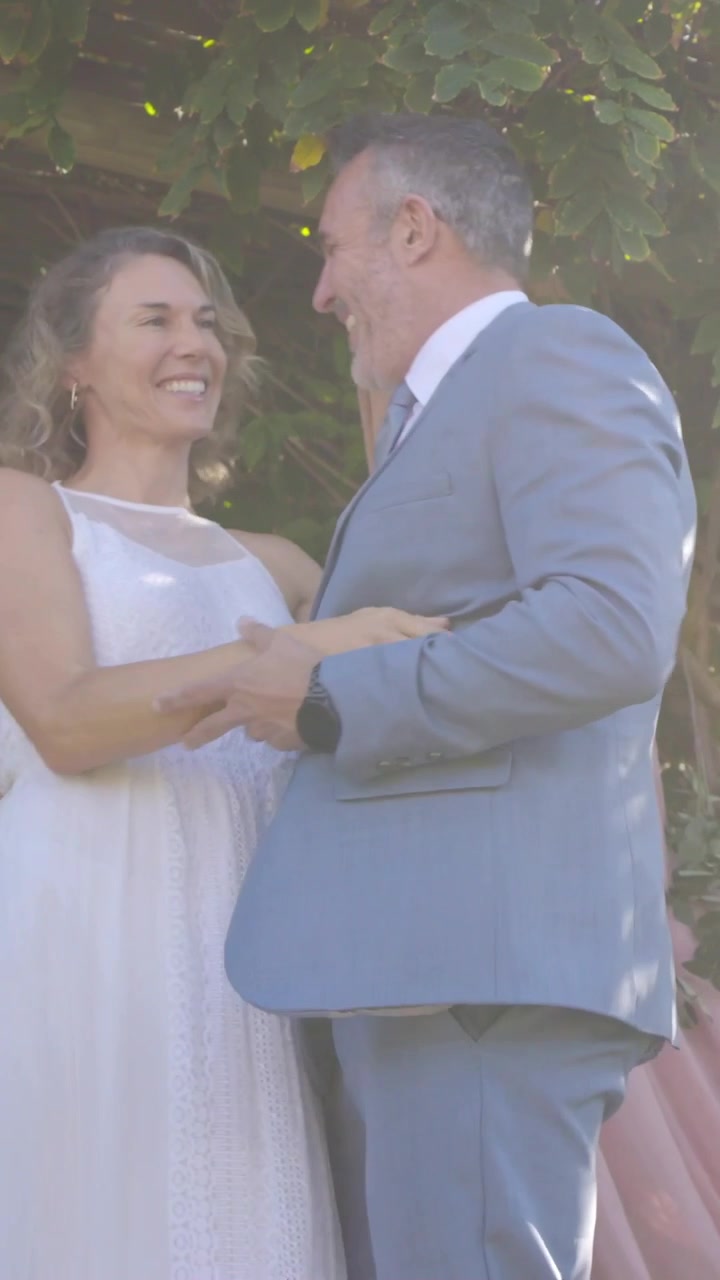 Vídeo vertical: Mulher estendendo a mão, homem virando e unindo as mãos em casamento no jardim, terno e vestido branco.