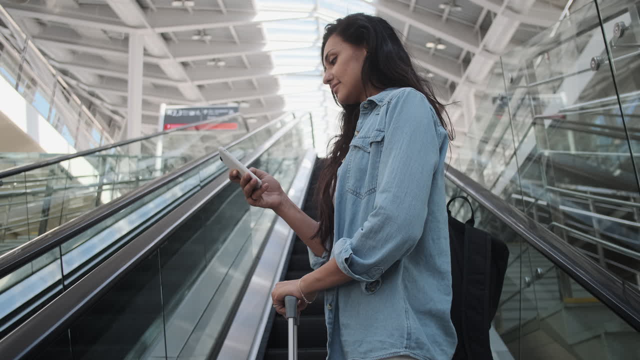 mujer usando el teléfono en la escalera mecánica del aeropuerto