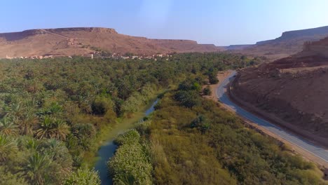 aerial flyover road beside palm tree and tranquil river in morocco during sunny day - desert mountains