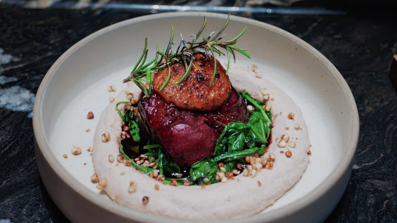 Close up of a gourmet dish featuring grilled steak topped with foie gras, served with sauteed spinach and a rosemary garnish