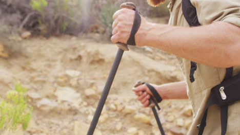 midsection of caucasian male survivalist trekking through wilderness with backpack and walking poles