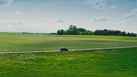 aerial pushing back from a blue bmw driving down a scenic road surrounded by lush green meadows in this stunning drone footage