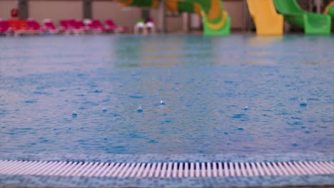 Close-up-slow-motion-shot-of-droplets-of-rain-falling-into-a-swimming-pool