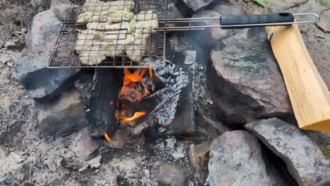 Outdoor-cooking-meat-under-flaming-hot-charcoal-fire-wood-camping-outdoor